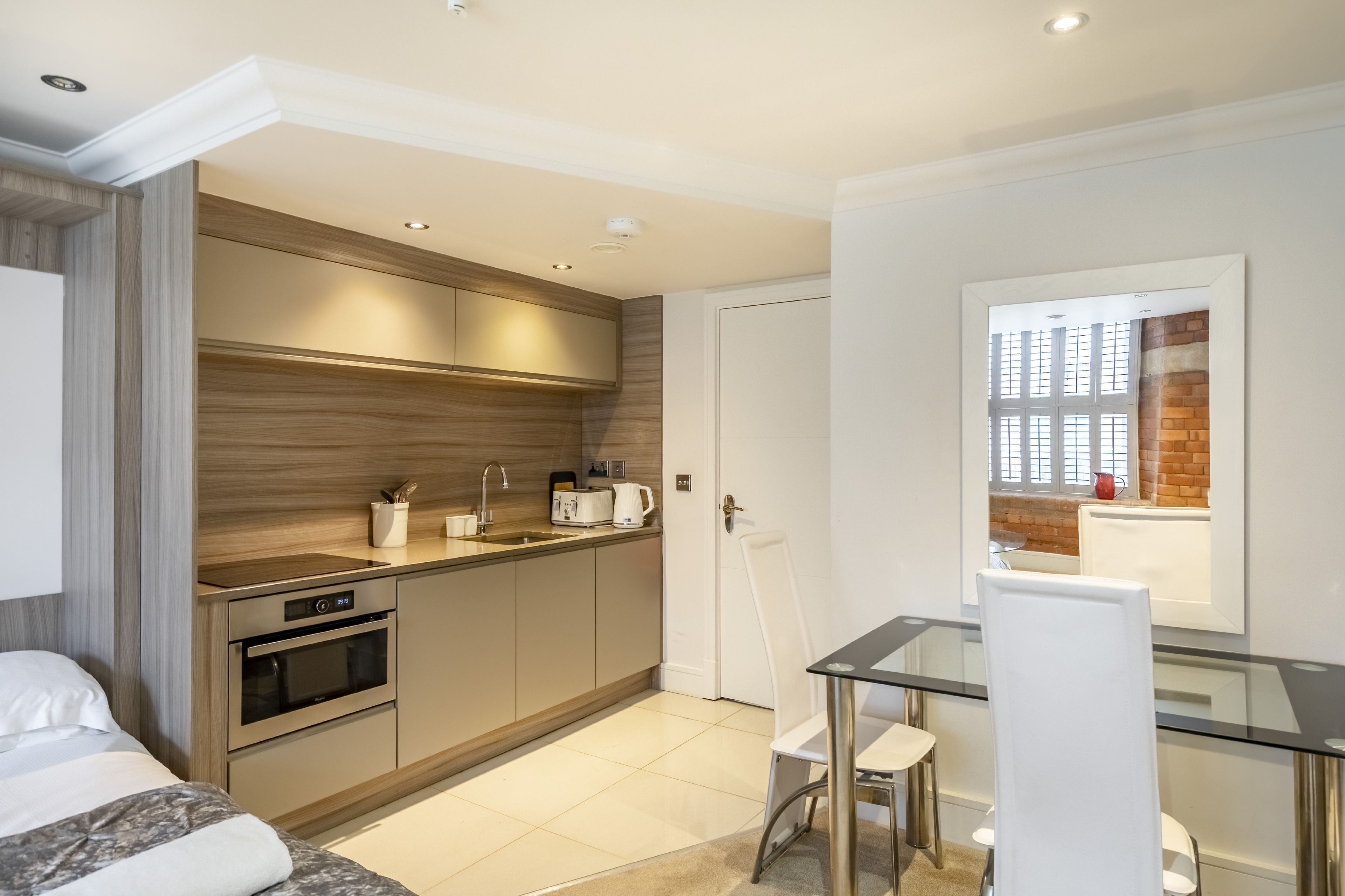 A modern kitchen with built-in appliances, a dining area with a glass table, and a view through a window.
