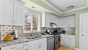 Una cocina con armarios blancos, estufa de acero inoxidable y salpicadero decorativo.