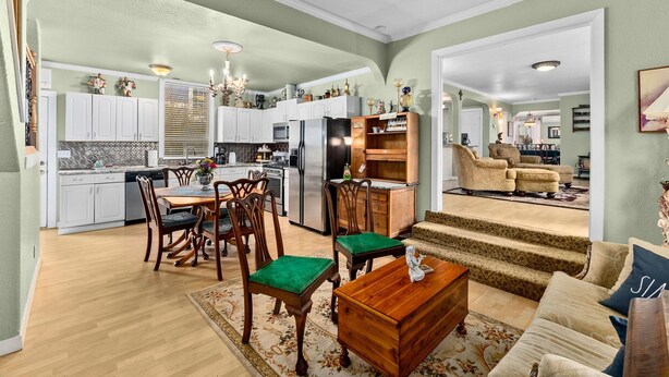 Un amplio espacio de sala con una mesa de comedor, sillas y un sofá. Se ve una cocina con gabinetes blancos y un refrigerador al fondo.