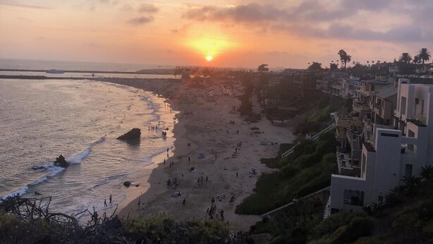 Uma praia com um pôr do sol, edifícios ao longo da costa e um céu claro.