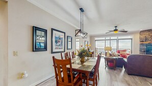 A dining area with a wooden table and chairs, a ceiling fan, and a large window with a view. - Close-to-slopes condo w/gourmet kitchen & stone fireplace (Sugar Mountain)