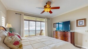 A bedroom with a large bed, a ceiling fan, a dresser, a television, and a balcony with a chair. - Close-to-slopes condo w/gourmet kitchen & stone fireplace (Sugar Mountain)