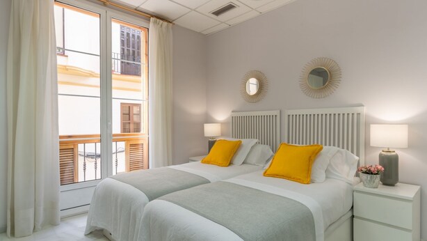 A hotel room with two beds, a white radiator, two bedside tables with lamps, and a view of a building through the window. - iloftmalaga Strachan-Larios (Málaga)