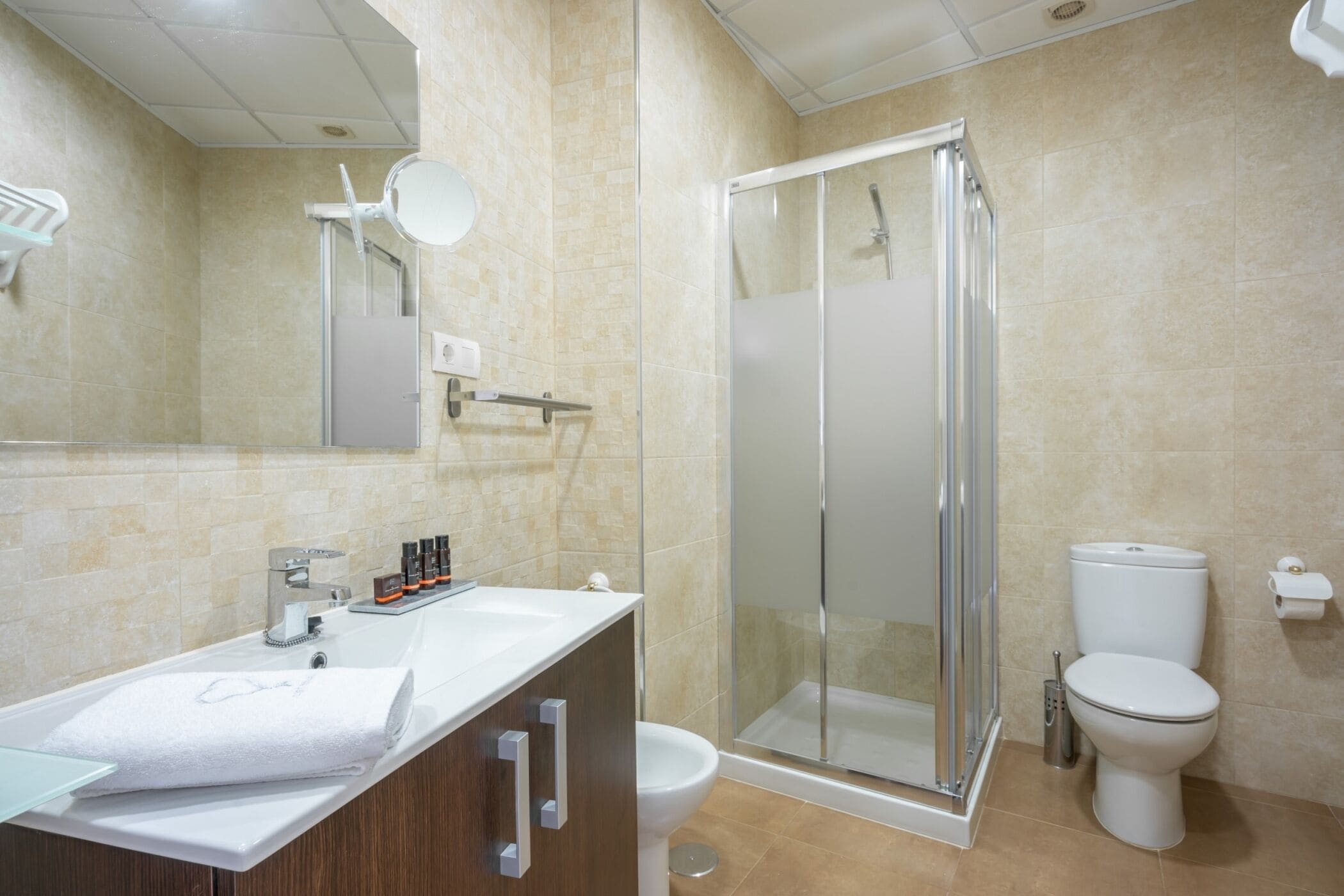 Un baño moderno con cabina de ducha de vidrio, inodoro blanco y tocador con espejo y artículos de aseo.