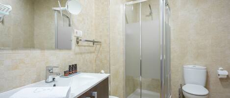 Un baño moderno con cabina de ducha de vidrio, inodoro blanco y tocador con espejo y artículos de aseo.