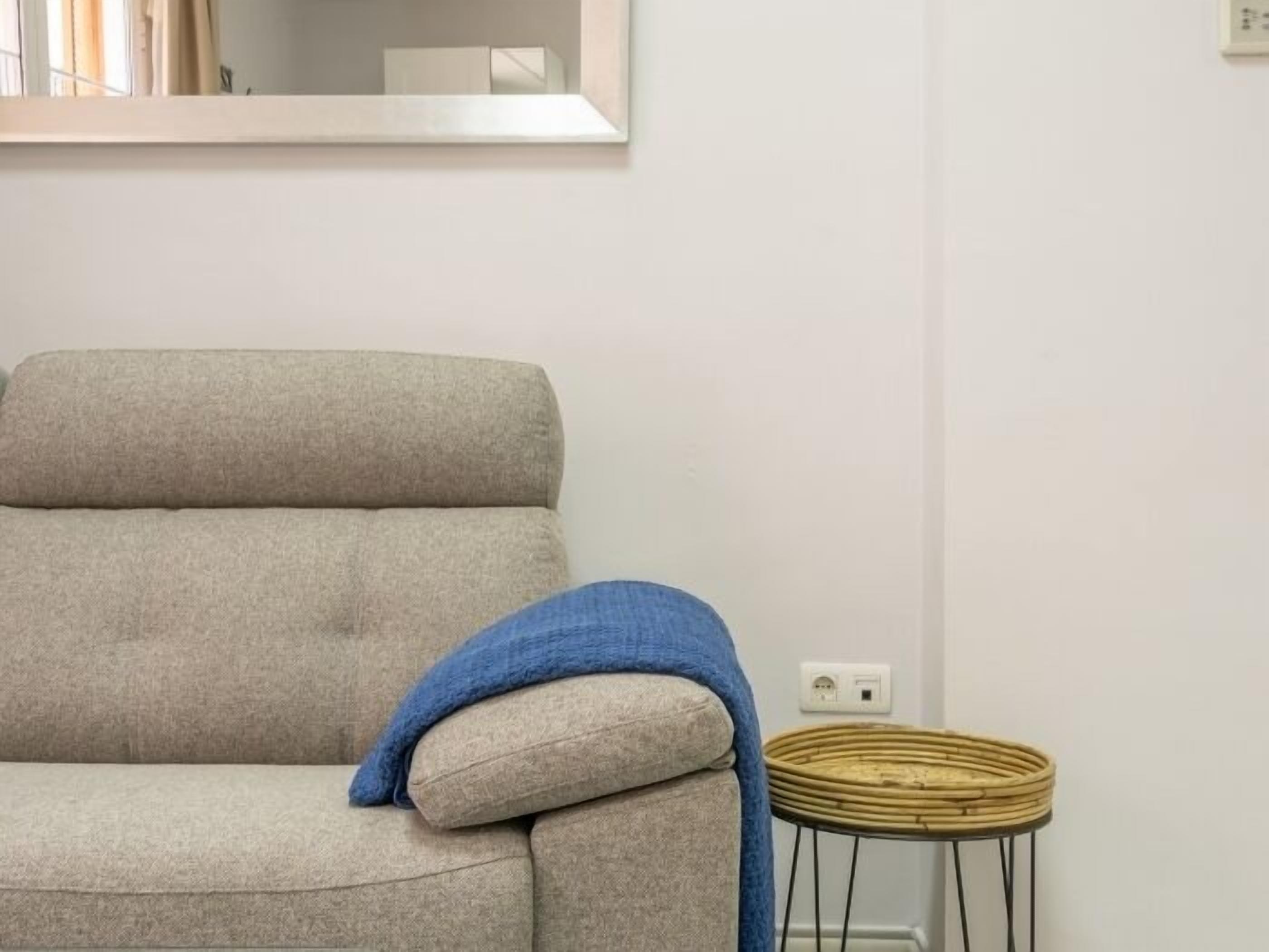 Un canapé aux couleurs neutres, agrémenté d’un plaid bleu et d’un tabouret en osier.