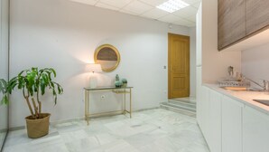 A hallway with a potted plant, a round mirror, a small table with a lamp, and a wooden door. - iloftmalaga Strachan-Larios (Málaga)