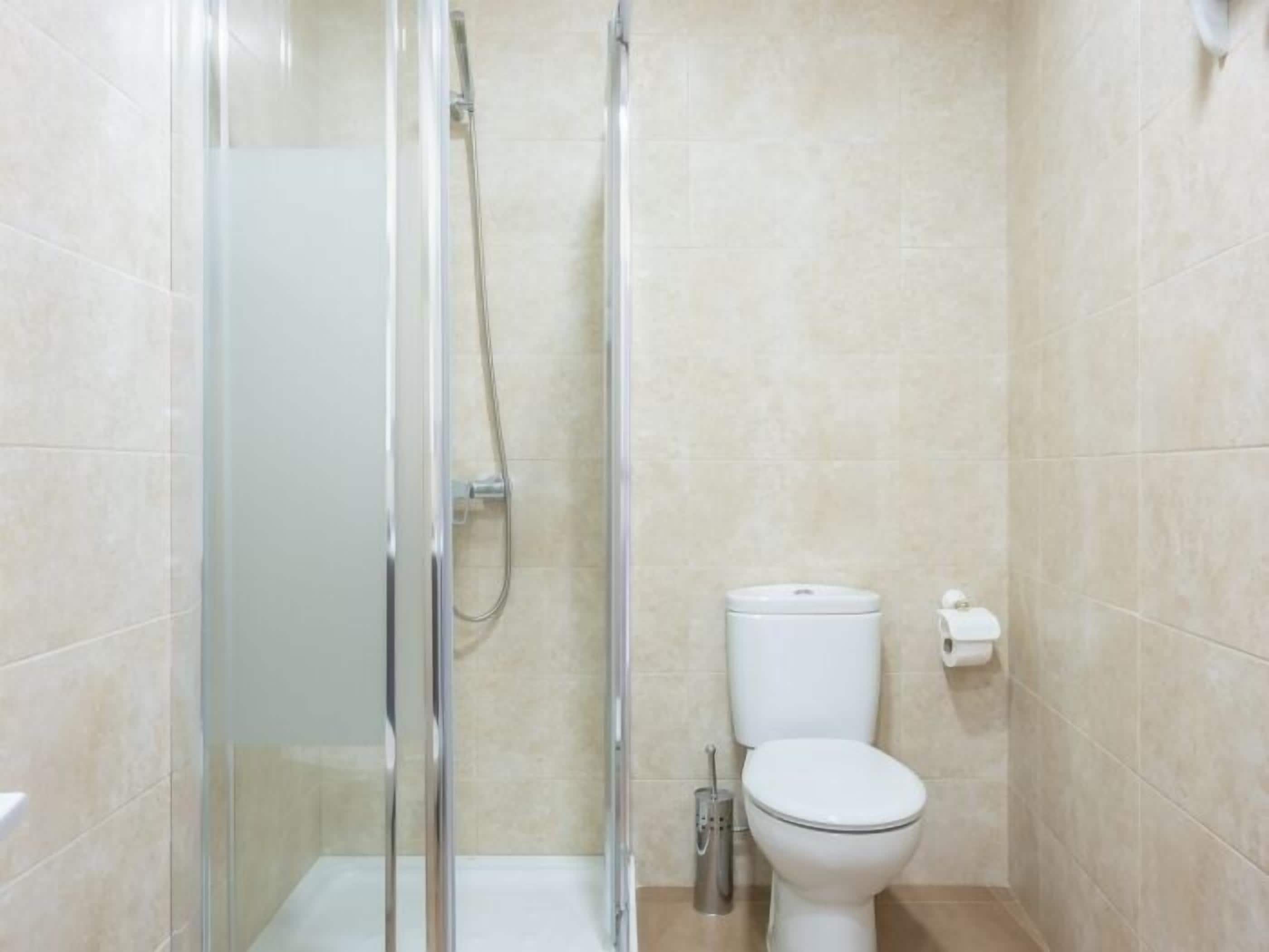 A small, modern bathroom with a glass-enclosed shower, a toilet, and a hand dryer.
