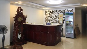 A reception area with a wooden reception desk, a clock, a decorative wall, and a refrigerator.