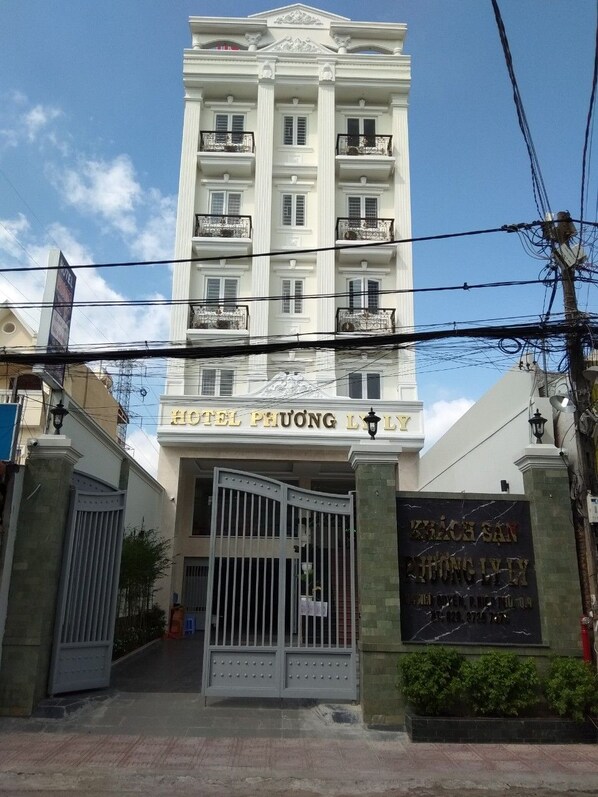 Un hôtel à plusieurs étages, doté d’une entrée imposante, d’une allée bordée de portails et d’une enseigne indiquant le nom de l’hôtel.