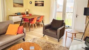 Un salon comprenant un canapé, un fauteuil, une table basse, une table à manger avec des chaises, et une vue sur l’extérieur grâce à une porte coulissante.