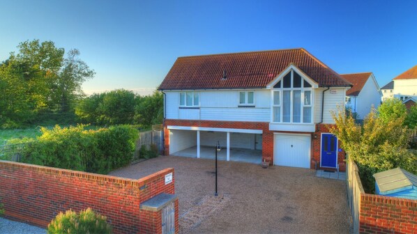 A two-story house with a garage, surrounded by a gravel driveway and a brick wall.