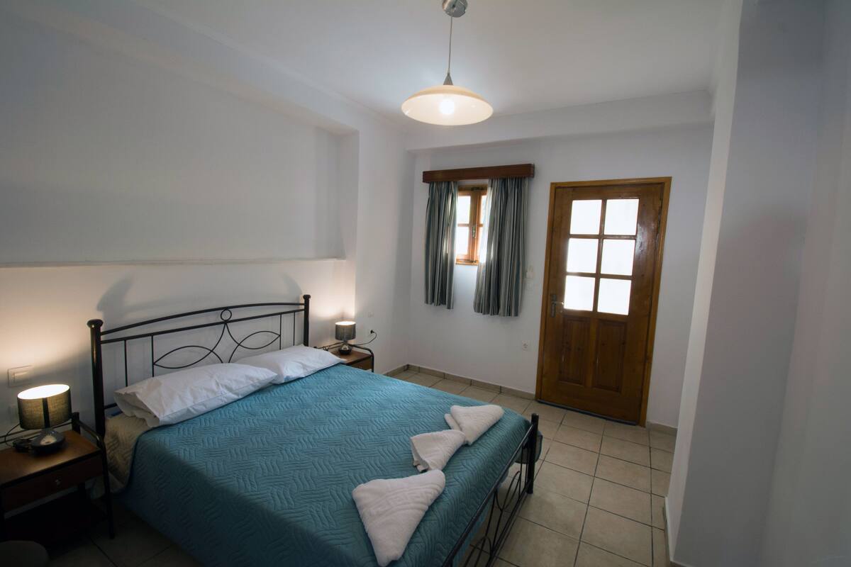 A bedroom with a bed, bedside lamp, and a wooden door.