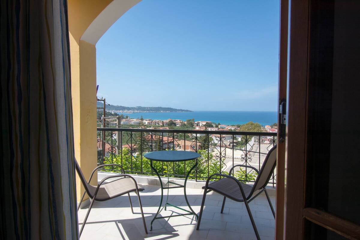 A balcony with a table and chairs, overlooking a coastal view.