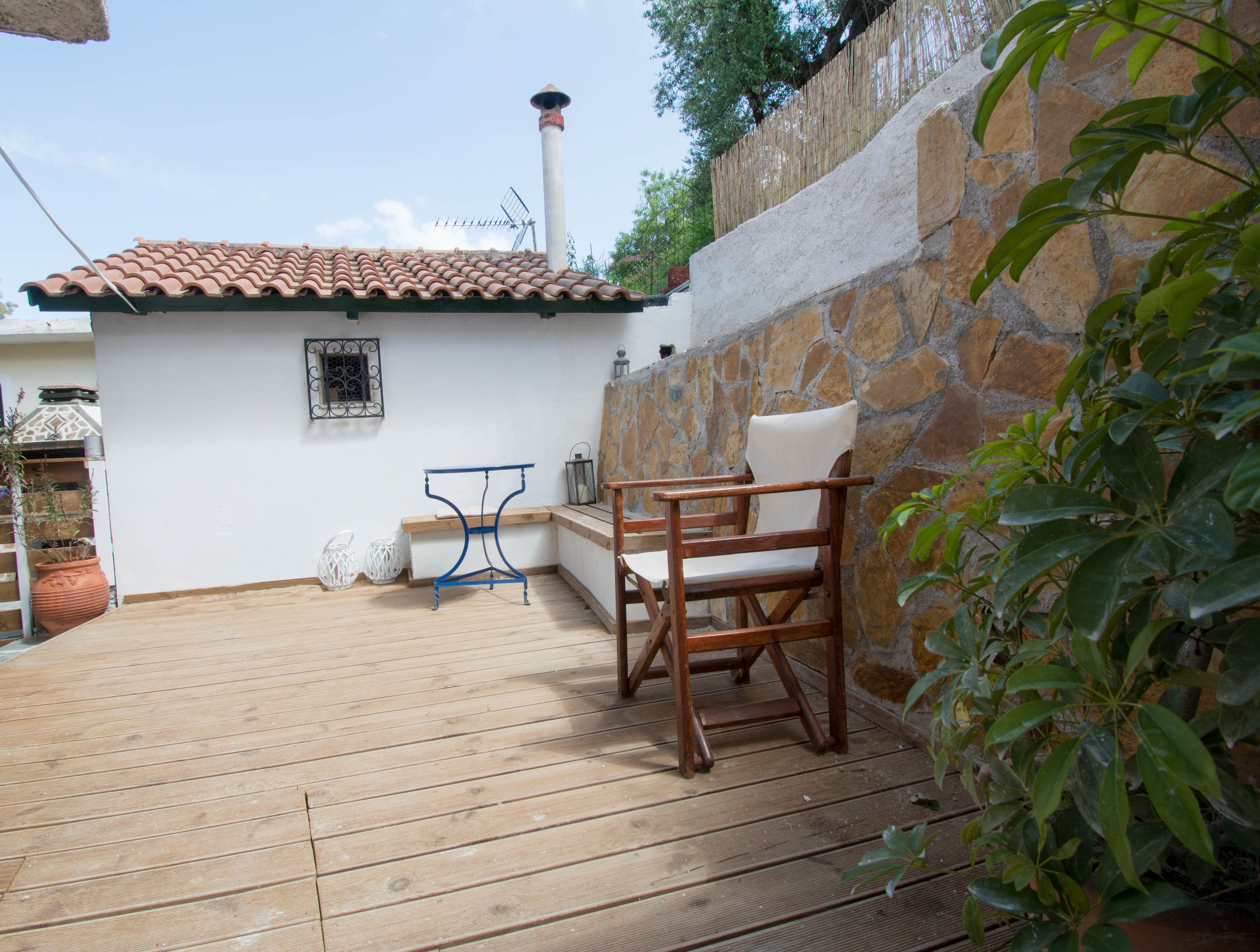 A wooden deck with a stone wall, a small table, and a chair.