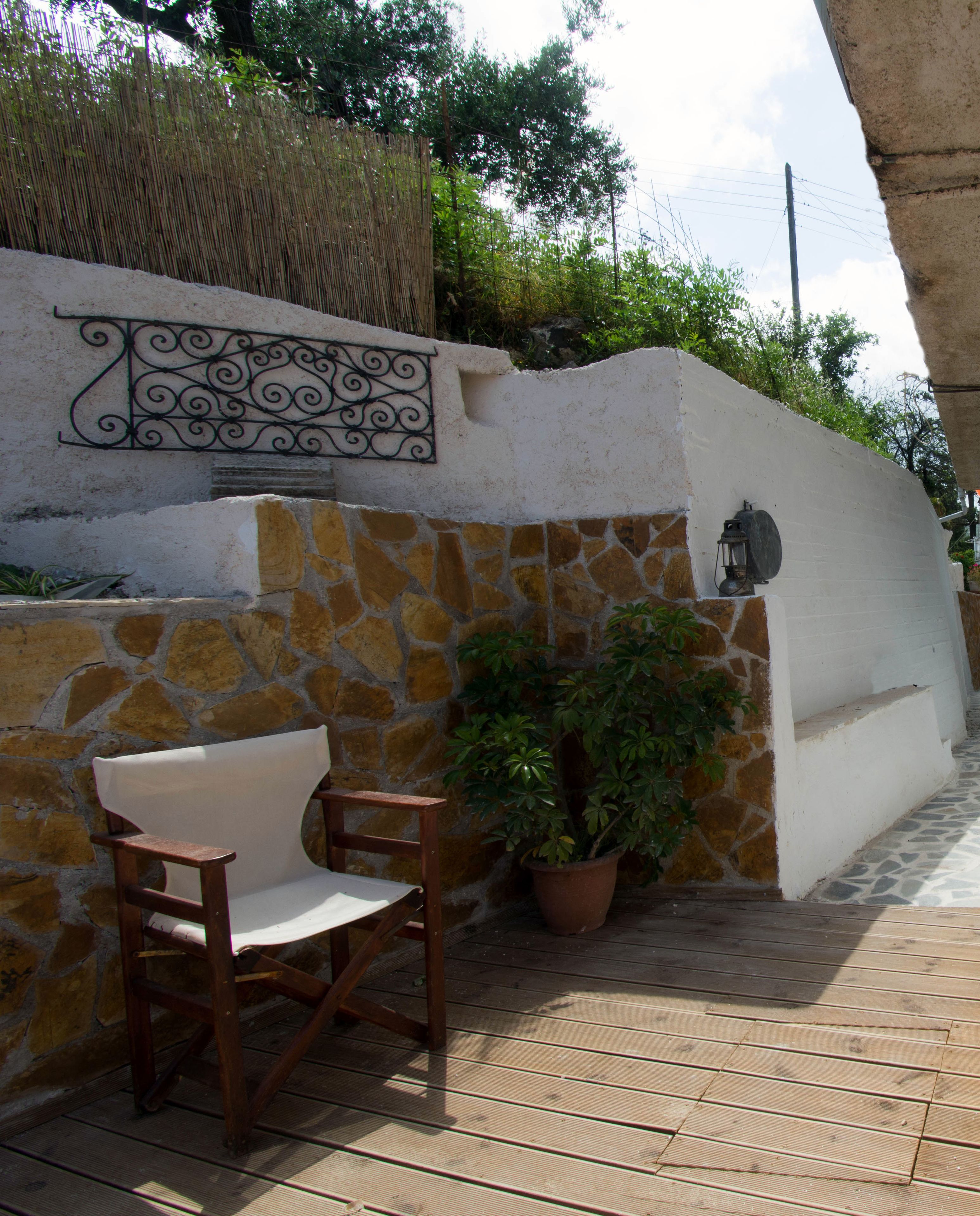 A stone wall with a decorative metal railing, a wooden chair, and a potted plant.