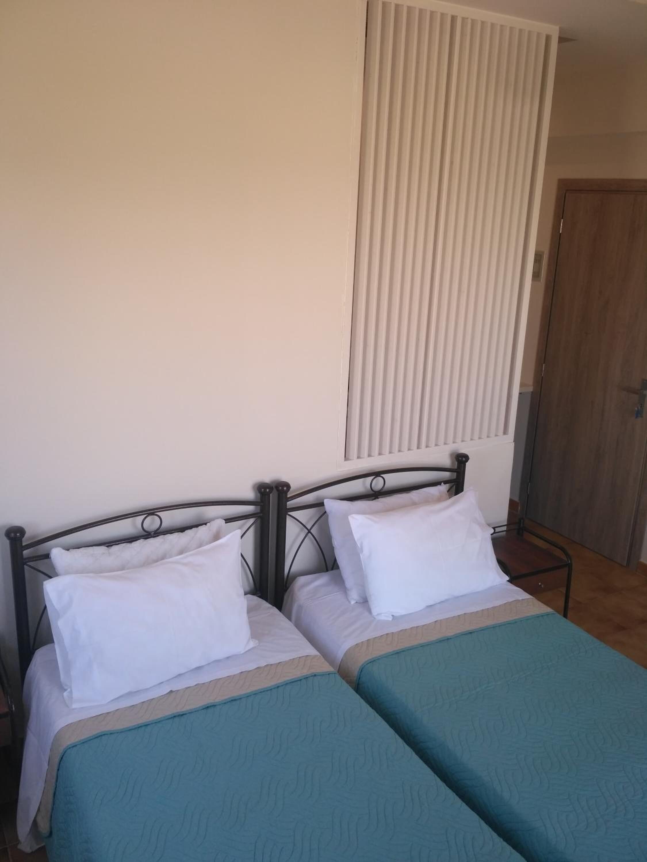 A room with two single beds, a wooden door, and a window with blinds.