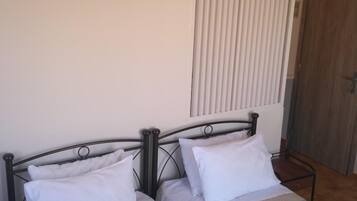 A room with two single beds, a wooden door, and a window with blinds.
