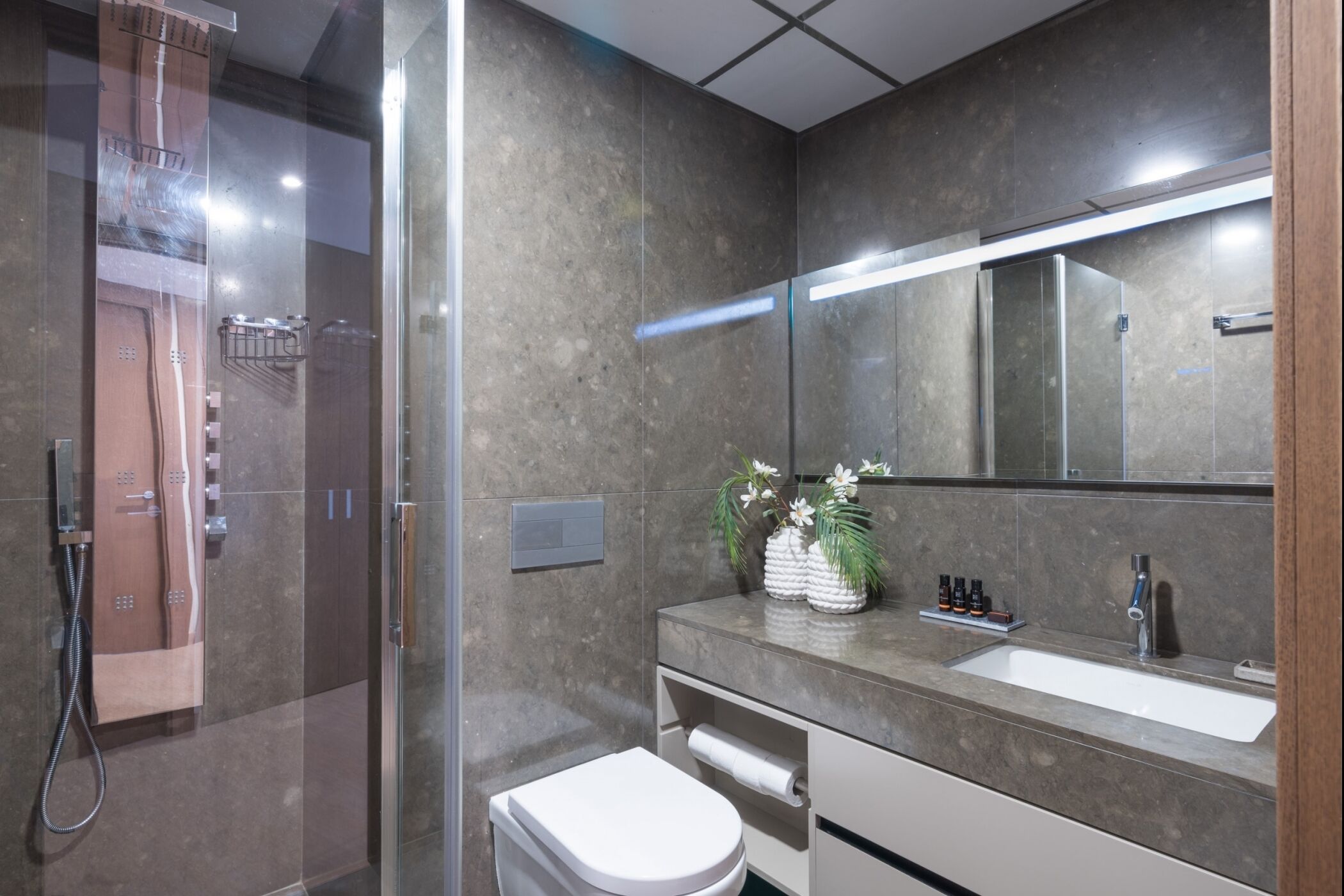 A modern bathroom with a glass-enclosed shower, a white toilet, and a vanity with a large mirror.