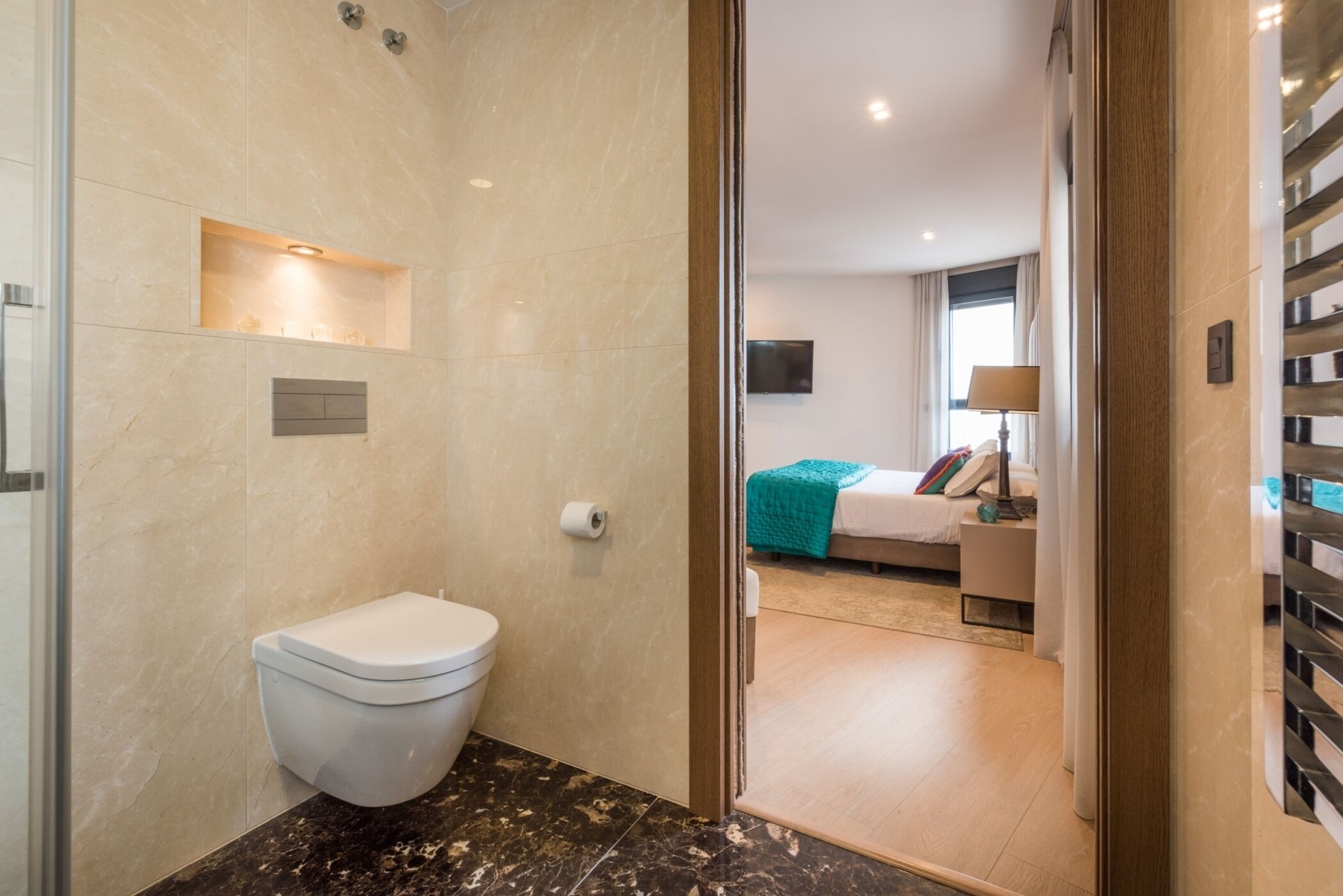 Une salle de bain moderne équipée de toilettes, d’une douche et d’une porte en verre donnant sur une chambre.