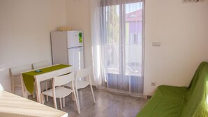 A small, clean room with a kitchenette, a dining table with chairs, and a green couch. - DreamDay apartment (Vir)