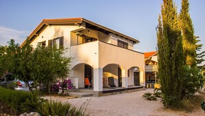 A two-story house with a white facade, a red-tiled roof, and a gravel driveway. There are two visible arches on the ground floor, and a balcony on the upper floor. - DreamDay apartment (Vir)