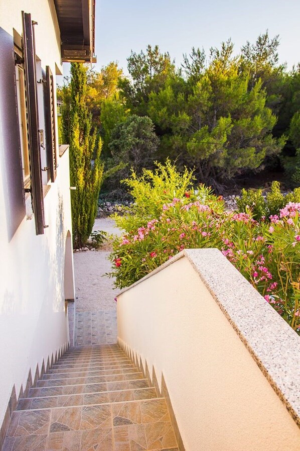 A stone staircase leading to a white building with a garden featuring pink flowers and green shrubs.