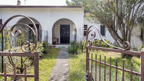 A rustic house with a paved pathway leading to an arched entrance, surrounded by greenery and a metal gate. - M224 - Marcelli, three-room apartment with garden 150m from the sea (Marcelli)