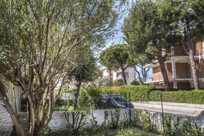 A residential area with a tree-lined street, a parked car, and a building with balconies. - M224 - Marcelli, three-room apartment with garden 150m from the sea (Marcelli)