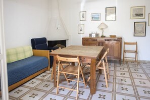 A room with a wooden table, chairs, a sofa, a cabinet, and tiled flooring.