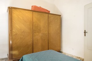 Una habitación con un armario de madera, una cama con colcha estampada y una puerta blanca.