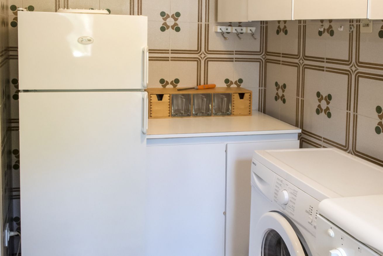 A compact kitchen with a refrigerator, a washing machine, and a wooden utensil holder.
