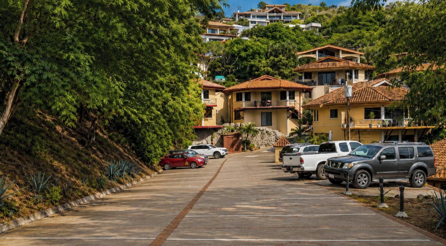 A residential street with parked cars and houses with tiled roofs.