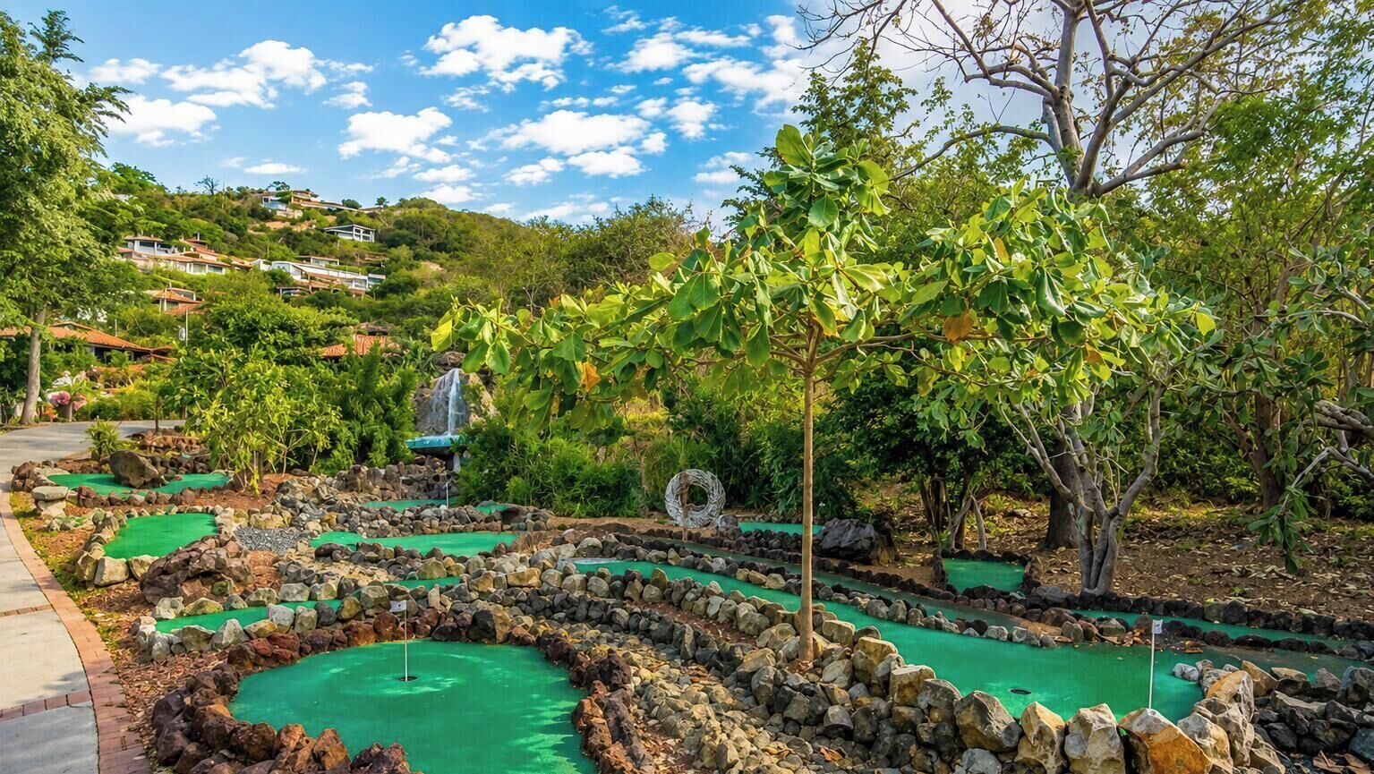 A miniature golf course with multiple holes, surrounded by greenery and a hilly landscape in the background.