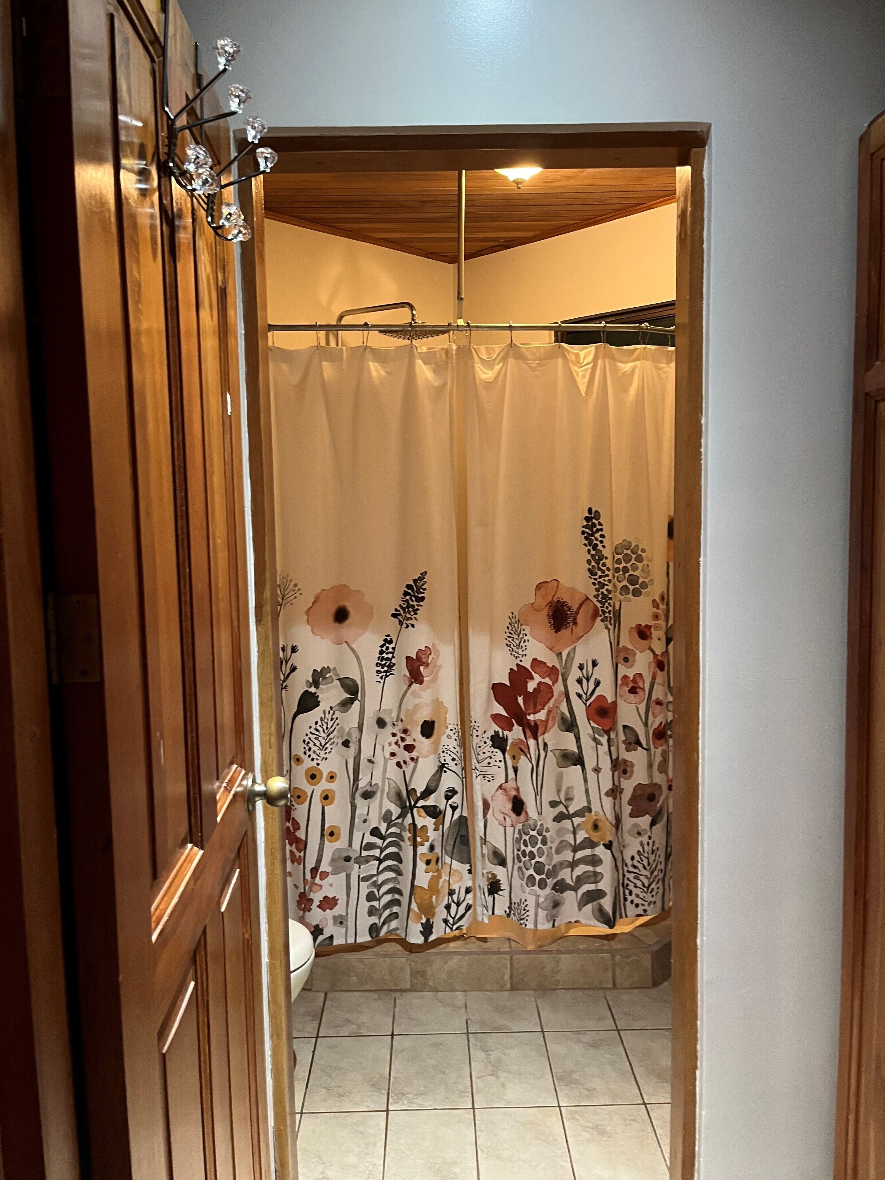 A bathroom with a shower curtain featuring a floral pattern, wooden doors, and a tiled floor.