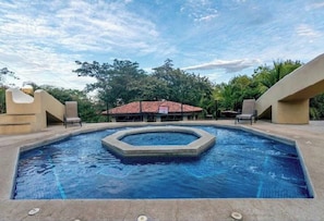 A swimming pool with a central circular feature, surrounded by lounge chairs and a building with a red-tiled roof in the background. - Your Comfortable, Safe, Updated Villa Retreat for 2 to 6 Guests in Playa Hermosa (Playa Hermosa)