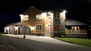 Une maison à deux étages avec une tour en pierre, plusieurs portes de garage et une allée bien éclairée.