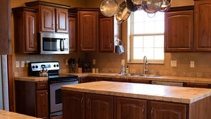 Une cuisine dotée de meubles en bois, d’un réfrigérateur en acier inoxydable, d’un four à micro-ondes, d’une cuisinière et d’un grand îlot central avec un évier.