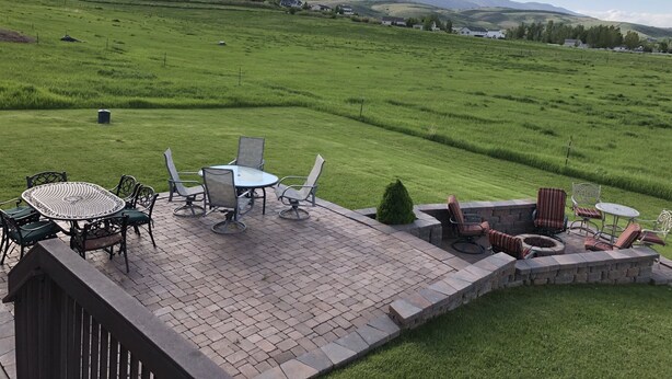 Une terrasse avec des meubles d’extérieur, un mur en pierre et une vue sur un champ verdoyant et des maisons éloignées.