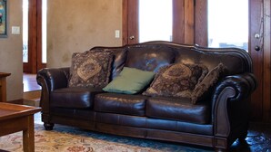 Un canapé en cuir marron agrémenté de coussins à motifs, une porte en bois et un tapis à motifs dans une pièce aux murs de couleur beige.