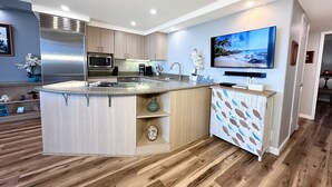 Una cocina moderna con una isla central, electrodomésticos de acero inoxidable y un televisor de pantalla plana sobre la isla.