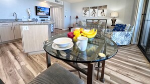 Una cocina moderna con una mesa de comedor de cristal, horno integrado y un televisor montado en la pared.
