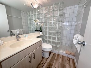 Un baño moderno con un espejo grande, un lavamanos color beige, un inodoro y una cabina de ducha de vidrio.