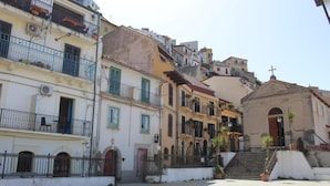 A narrow street with buildings on both sides, a small church with a cross on top, and a staircase leading up to the church. - Sea Side Rooms (Scilla)