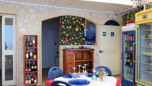 A dining area with a stone wall, a wooden cabinet with bottles, a table set for two with blue plates, and a vintage refrigerator. - Sea Side Rooms (Scilla)