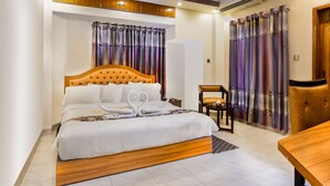 A neatly arranged bedroom with a large bed, a wooden headboard, and a bedside table. - Memento International (Dhaka)