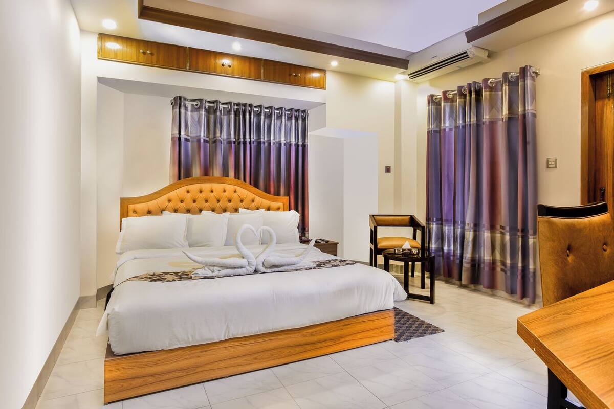 A hotel room with a large bed, a wooden headboard, a bedside table, a chair, and a small table.