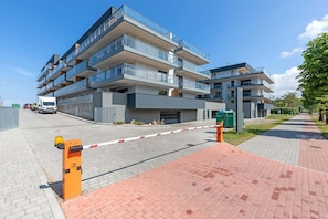 Un moderno edificio de apartamentos con varios balcones, una entrada con reja y un camino pavimentado.
