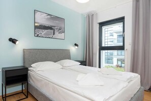 A bedroom with a bed, a nightstand, a wall-mounted picture, and a window with curtains. - Bright Apartment with Sea View | Close to the Beach and Parking (Dziwnów)