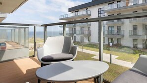 Een modern balkon met glazen omheining, een grijze stoel met kussens en een kleine tafel.